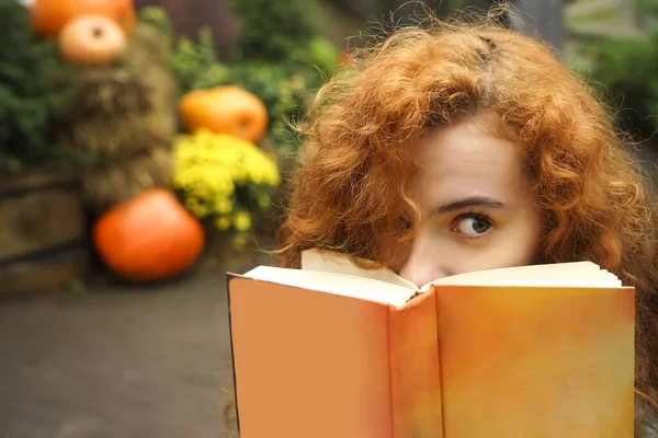 Belle Étudiante Rousse Bouclée Couvrant Son Visage Derrière Livre Orange — Photo