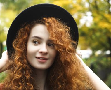 Ormanda siyah şapkalı hoş bir genç kız gün batımında arka planda ve uzaklara bakıyor. kızıl saçlı kıvırcık kadın siyah şapka takıyor.