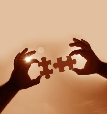 Gökyüzü arka planında yapboz parçaları olan eller.  