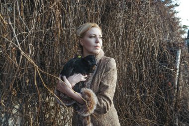 Orta yaşlı, zarif, modaya uygun, kürklü bir kız elinde siyah bir kuş tutuyor. Güzel evcil hayvanı olan şık bir kadın. Siyahlı kadın ve kuş tavuğu tünelde. Hayvan sever. Yeni akış yaşam biçimi