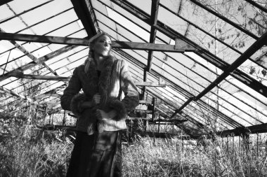 Sarışın, orta yaşlı bir kadın terk edilmiş bir serada, kurumuş çalılar ve kuru uzun otlar içinde.. 