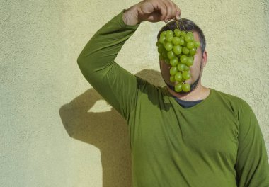 Sakallı bir adam elinde bir demet yeşil üzüm tutuyor