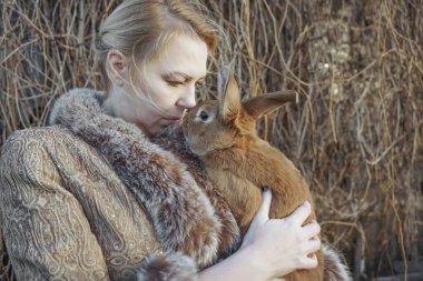 Sarışın kadın sevimli pofuduk tavşan tutuyor, yakın çekim görüntüsü. Kış mevsimi. Orta yaşlı kadın kucağında sevimli kahverengi bir tavşan tutuyor.. 