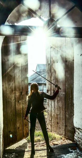 blond woman warrior with a sword standing  on old, retro, vintage, aged opened door background. medieval female elf with sword looking inside church