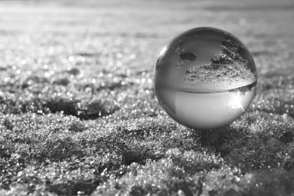 Glass globe lie on dirty snowdrift or ice  background with sun rays. Planet earth globe with continents figurine on sea. Glass Globe, Glass globe decoration. blurred snow background.