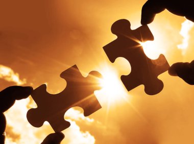 Gökyüzü arka planında yapboz parçaları olan eller.  