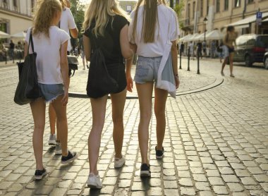 Avrupa 'da yaz aylarında dört güzel, mavi kot pantolonlu sarışın kadın kısa yürüyüşler yapıyor. Tam boy. Yaz şehrinde uzun bacaklı, şortlu seksi kızlar takımı. Güneşli ışık kaldırım taşında.