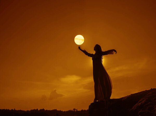 Silhoutee of woman standing on top of mountain. female hold in hand growing moon above forest trees. backlight and moon light.