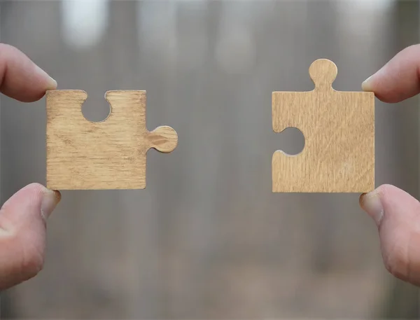 two hands person trying to connect couple Jigsaw wooden puzzle piece with trees  background.