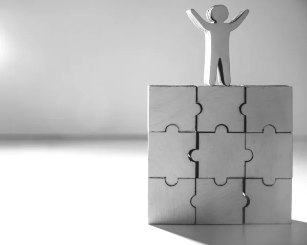 assembling blank white puzzles in house shape on white background. human wooden figure with hands up.