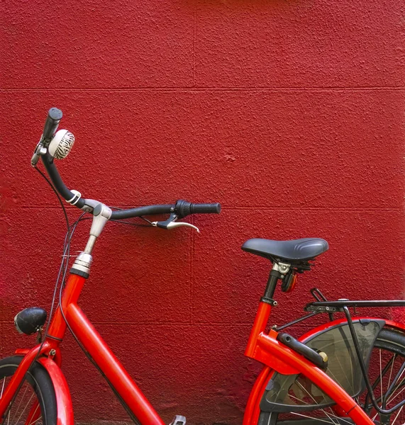 Ein rotes Fahrrad, das vor einem Reihenhaus zwischen zwei Fenstern abgestellt war — Stockfoto