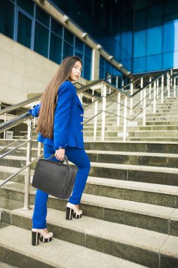 Güzel, esmer Asyalı kadın yürürken ya da aşağıya koşarken arkasına bakıyor. Kariyer kavramı - merdivenlerde yalnız genç bir iş kadını. İş kadını mavi takım elbise giyer..