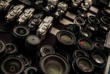 Renkli yansıma önleyici çok katmanlı birçok fotoğraf lensinin yakın çekimi. Masadaki kameralar farklı marka. Objektifle hedefin arkaplanı