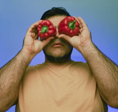 Yüzüne büyük kırmızı biber tutan bir adamın komik bir fotoğrafı. beyaz veya gri arkaplanda izole edilmiş. 