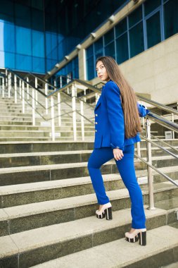 Güzel, esmer Asyalı kadın yürürken ya da aşağıya koşarken arkasına bakıyor. Kariyer kavramı - merdivenlerde yalnız genç bir iş kadını. İş kadını mavi takım elbise giyer..