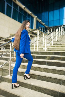 Güzel, esmer Asyalı kadın yürürken ya da aşağıya koşarken arkasına bakıyor. Kariyer kavramı - merdivenlerde yalnız genç bir iş kadını. İş kadını mavi takım elbise giyer..