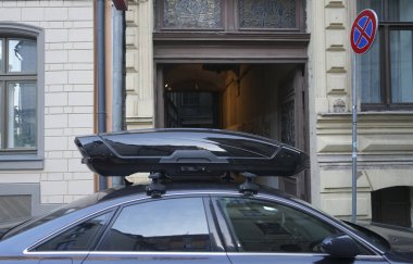Karanlık ve modern bir arabanın çatısında büyük siyah bir sandık. Ulaşım için seyahat ve aksesuarlar. Bagaj kutusu arabanın çatısına sabitlendi.