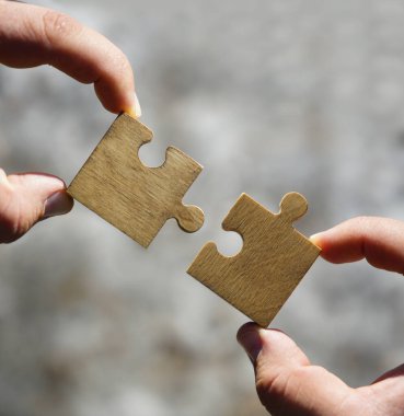 İki elli insan, arka planda ağaçlar olan bir çift yapboz parçasını birleştirmeye çalışıyor.. 