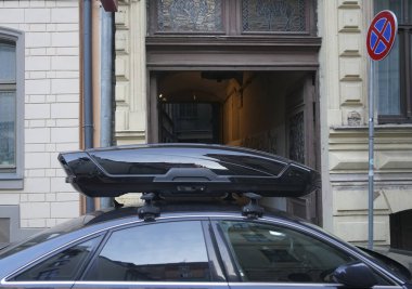 Karanlık ve modern bir arabanın çatısında büyük siyah bir sandık. Ulaşım için seyahat ve aksesuarlar. Bagaj kutusu arabanın çatısına sabitlendi.