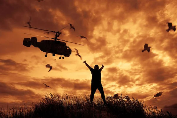 Silhouette eines Mannes, der mit erhobenen Händen aufspringt. Hubschrauber. Kampfhubschrauber fliegt über Kopf — Stockbild Silhouette Eines Mannes Der Mit Erhobenen Händen Aufspringt Hubschrauber Kampfhubschrauber — Stockfoto