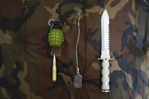 Knife, bullet, pineapple and army token on the background of camouflage. stainless steel. khaki backdrop.