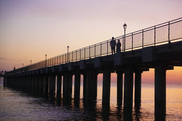 新的现代桥上升起了五彩缤纷的日出 波罗的海 日落时的新桥 走在路上的一对浪漫情侣的轮廓 — 图库照片