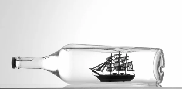 Miniature tall ship with sails rigged in a clear glass bottle displayed over a white background in a nautical theme