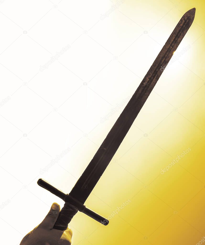 historical sword in male hand on blue sunny sky background. no face. sun rays.