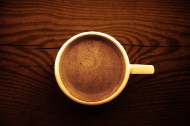 Kahverengi ahşap yüzey arka planında güzel köpüklü beyaz seramik kahve kapağı. 