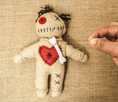 vintage voodoo doll on textile material  background. male hand sticks a doll with a needle