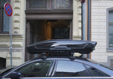 Karanlık ve modern bir arabanın çatısında büyük siyah bir sandık. Ulaşım için seyahat ve aksesuarlar. Bagaj kutusu arabanın çatısına sabitlendi.