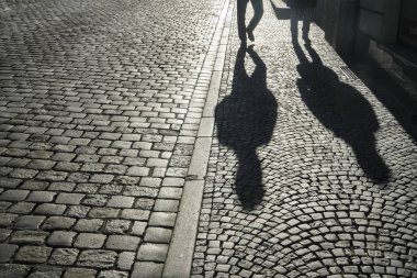 Clear shadows of people on a cobblestone pavement. european  pedestrian street in sunset light in summer evening. Black and white. homosexual couple of gays. 