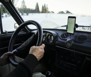 İçinde GPS ekranı olan antika bir arabanın görüntüsü açık, güneşli bir günde, arka planda karlı dağlarla kaplı düz bir buz yolunda direksiyonda sürücü erkek eli var.