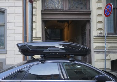 Karanlık ve modern bir arabanın çatısında büyük siyah bir sandık. Ulaşım için seyahat ve aksesuarlar. Bagaj kutusu arabanın çatısına sabitlendi.