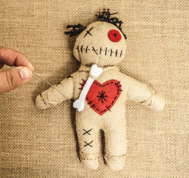 vintage voodoo doll on textile material  background. male hand sticks a doll with a needle