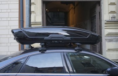 Karanlık ve modern bir arabanın çatısında büyük siyah bir sandık. Ulaşım için seyahat ve aksesuarlar. Bagaj kutusu arabanın çatısına sabitlendi.