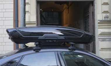 Karanlık ve modern bir arabanın çatısında büyük siyah bir sandık. Ulaşım için seyahat ve aksesuarlar. Bagaj kutusu arabanın çatısına sabitlendi.