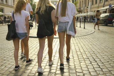 Avrupa 'da yaz aylarında dört güzel, mavi kot pantolonlu sarışın kadın kısa yürüyüşler yapıyor. Tam boy. Yaz şehrinde uzun bacaklı, şortlu seksi kızlar takımı. Güneşli ışık kaldırım taşında.