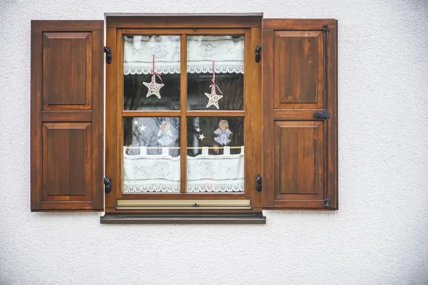 Wooden brown window shutters. Window on a white wall with dark shutters.