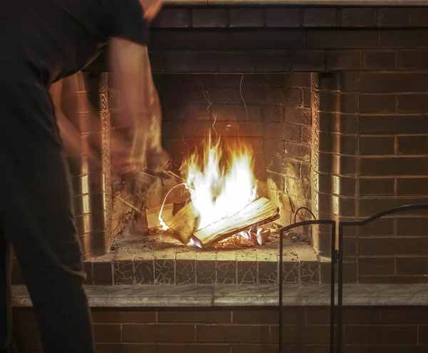暖かいローブに身を包んだ男が近代的な暖炉の薪を燃やして — ストック写真