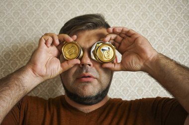 Duvarında 3 tane alüminyum bira kutusu olan evsiz sakallı bir adam. Altın kutu gözler ve ağızdan önce gelir..