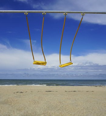 Arka planda okyanus olan iki boş salıncak. Bunlar bebekler için metal salıncaklar. Salıncak bir çocuğun düşmesini engelleyebilir. 