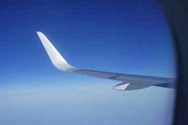  Gökyüzüne bakan uçak penceresi ve uçak kanadı. Mavi gökyüzündeki lombozdan bir yolcu uçağının kanat görüntüsü.