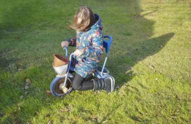 Mavi renkli, üç tekerlekli, paslı tekerlekli çocuk ve küçük kız çocuğu. bahar yeşili çayır. Rüzgarlı hava. 
