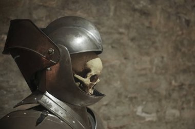 Gri arka planda şövalye miğferi takmış insan kafatası.