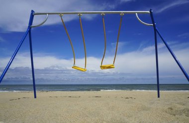 Arka planda okyanus olan iki boş salıncak. Bunlar bebekler için metal salıncaklar. Salıncak bir çocuğun düşmesini engelleyebilir. 