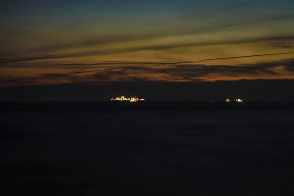雲に覆われたオレンジ色の空の明るい終わりの光は 日没時に海上を航海する大きな貨物船のシルエットを彫刻しています — ストック写真