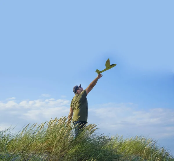 man  playing  with a model airplane on blue cloudy sky background. Dream to be a pilot. male standing on peak of hill.