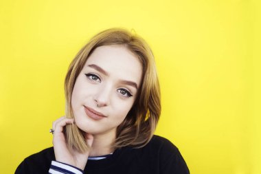 Uzun saçlı, siyah kazaklı, sarı arka planda duran genç bir kız..