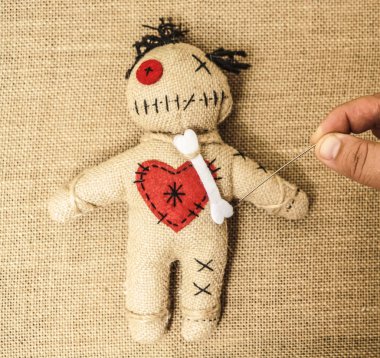 vintage voodoo doll on textile material  background. male hand sticks a doll with a needle